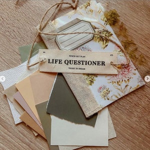Pode incluir: Uma cole&ccedil;&atilde;o de artigos de papelaria, incluindo um caderno com padr&atilde;o floral, v&aacute;rias amostras de papel em tons neutros e uma etiqueta que diz "LIFE QUESTIONER". Os itens s&atilde;o amarrados com barbante, criando um arranjo visualmente atraente.