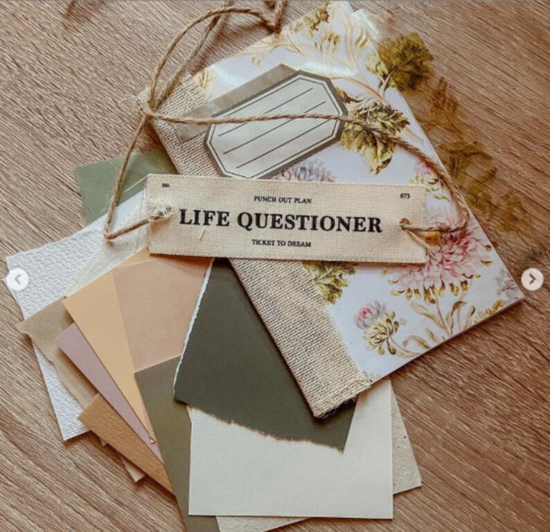 Pode incluir: Uma cole&ccedil;&atilde;o de artigos de papelaria, incluindo um caderno com padr&atilde;o floral, v&aacute;rias amostras de papel em tons neutros e uma etiqueta que diz "LIFE QUESTIONER". Os itens s&atilde;o amarrados com barbante, criando um arranjo visualmente atraente.