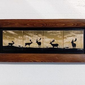 Op de afbeelding: Een ingelijst kunstwerk met vijf hertensilhouetten tegen een bewolkte, gouden lucht. De herten kijken in verschillende richtingen, wat een dynamische compositie creëert. Het kunstwerk is ingelijst in een donkerhouten lijst.