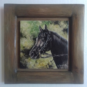 Puede incluir: Una pintura enmarcada de la cabeza de un caballo negro con una brida. El caballo está sobre un fondo verde y marrón con un efecto nublado. La pintura está firmada "Jim Foty" en la esquina inferior derecha.