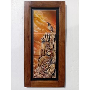 May include: A framed artwork featuring three partridges perched on a rocky cliffside against a sunset sky. The artwork is framed in a dark wood and has a black border around the tile image. The partridges are brown and white.