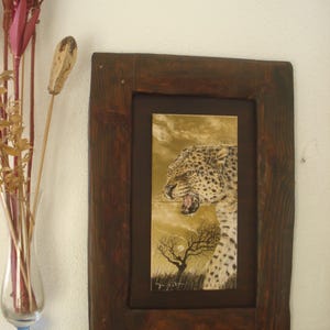 Może przedstawiać: Ilustracja w ramie przedstawiająca lamparta z warkoczącym wyrazem twarzy, na tle pustynnego krajobrazu z samotnym drzewem i pełnią księżyca. Dzieło jest podpisane "L. Past"