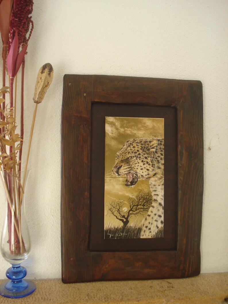 Może przedstawiać: Ilustracja w ramie przedstawiająca lamparta z warkoczącym wyrazem twarzy, na tle pustynnego krajobrazu z samotnym drzewem i pełnią księżyca. Dzieło jest podpisane "L. Past"