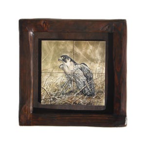 May include: A framed ceramic tile with a detailed painting of a falcon perched in a field of tall grasses. The tile is set in a dark wood frame.