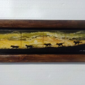 May include: A framed painting depicting five wolves running across a field at sunset. The sky is a blend of yellow, orange, and purple. The wolves are silhouetted against the sunset.