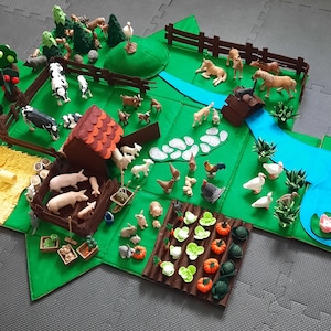 Op de afbeelding: Een vilt speelset voor kinderen met een boerderij scène met dieren, een huis, een rivier en een tuin. De set bevat een verscheidenheid aan boerderijdieren, waaronder koeien, varkens, kippen en eenden. Er zijn ook bomen, een hek en een klein huis. De set is perfect voor fantasierijk spelen en leren over het boerenleven.