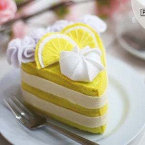 May include: A felt lemon cake slice with white frosting and purple felt flowers. The cake is on a white plate with a fork.