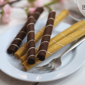 Op de afbeelding: Een wit bord met een vork en vijf chocolade- en vanillewafels. De rollen zijn in een kruispatroon gerangschikt.