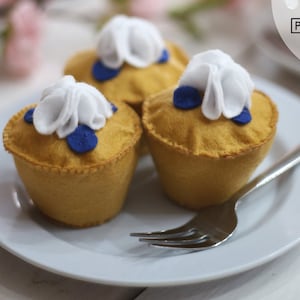 May include: Three felt blueberry pies with white whipped cream topping on a white plate with a silver fork.