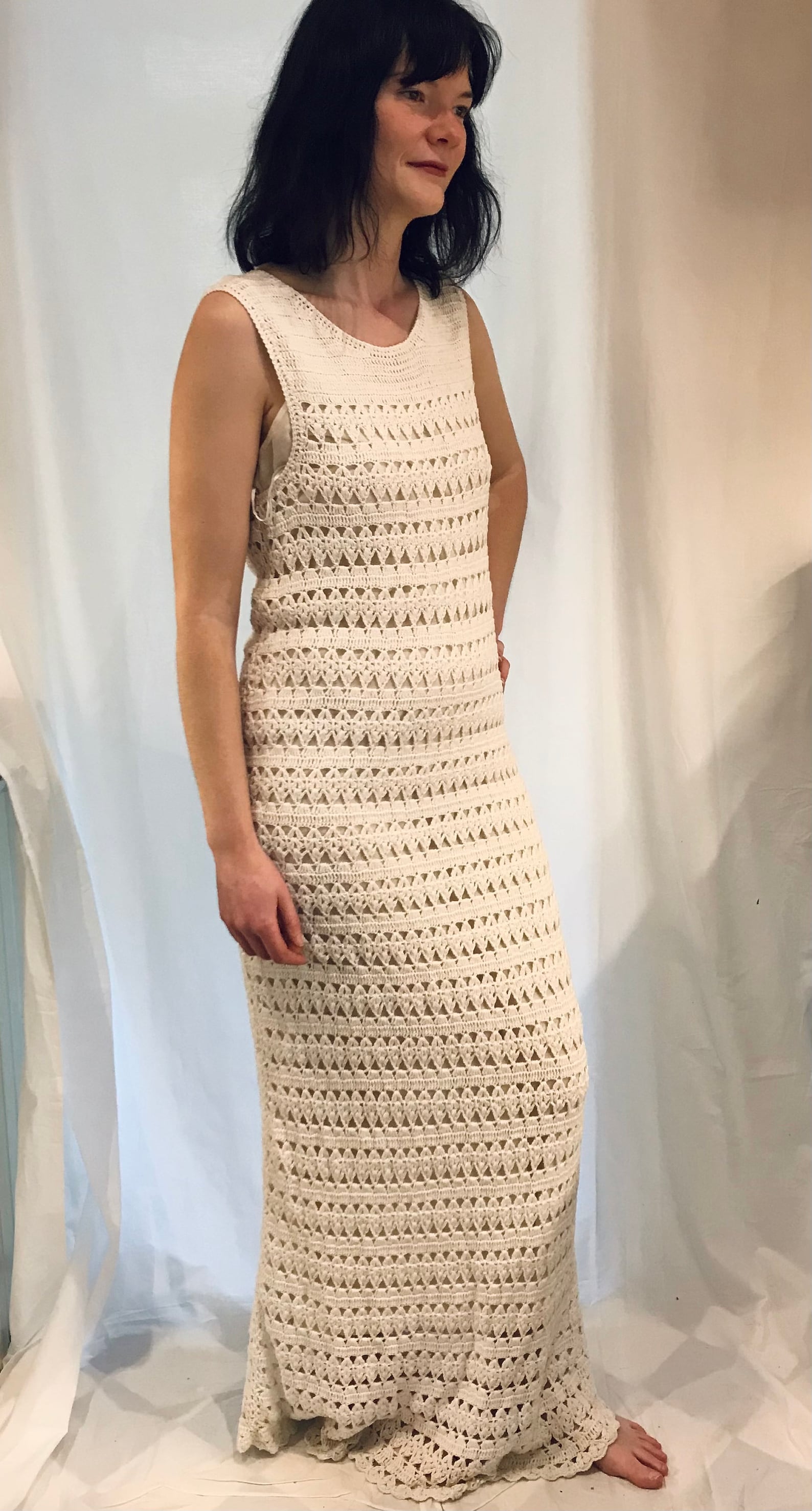 Cream sleeveless vintage crochet floor length maxi dress. Features back zipper, crochet fabric, a white polyester lining, a crew neckline and a crochet knitted fabric with a little stretch in it