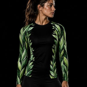 May include: A long-sleeved athletic shirt featuring a solid black centre panel and sleeves adorned with a vibrant green leaf pattern. The design includes a crew neckline and fitted silhouette, with the leaf print extending along the sides.
