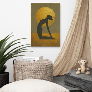 Könnte beinhalten: Ein Leinwanddruck mit einer Silhouette einer Person in einer Yoga-Pose vor einer goldenen Sonne. Das Kunstwerk verwendet eine neutrale Farbpalette mit Gold-, Braun- und Olivgrüntönen. Der Druck wird an einer weißen Wand angezeigt.