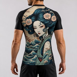 Op de afbeelding: Een sportshirt met korte mouwen en een grafische print op de achterkant. Het ontwerp toont een persoon met donkerblauw haar versierd met lichtroze bloemen, tegen een achtergrond van gestileerde blauwe oceaangolven en kersenbloesemtakken.