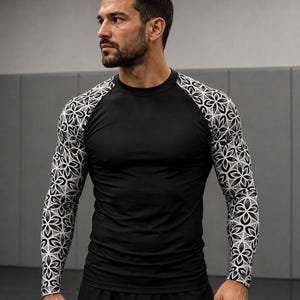 May include: A long-sleeve compression shirt featuring a solid black torso and sleeves adorned with a repeating white and black geometric flower pattern. The garment has a crew neckline and raglan-style sleeves that extend to the wrists.