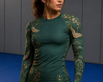 May include: A long-sleeved athletic top in dark green featuring a detailed print of flying cranes, floral patterns, and stylised clouds. The garment has a round neckline and a small gold emblem near the hem with a sun and mountain graphic.
