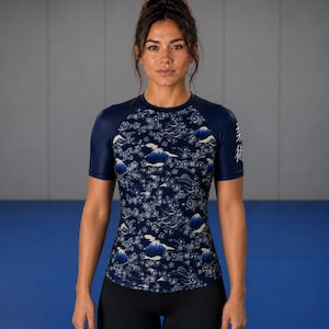 May include: Navy blue short-sleeve athletic shirt with a Japanese-inspired floral and mountain pattern. The shirt has dark blue sleeves and a crew neck. The Japanese characters are printed on the right sleeve. The person is wearing black leggings.