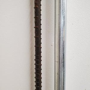 May include: Close-up of two metal rods against a white wall. One rod is dark brown and textured, with a series of raised ridges. The other is a smooth, silver-colored metal rod. The rods are vertical and parallel.