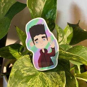 Puede incluir: Una pegatina con un personaje de dibujos animados con cabello negro, ojos azules y una camisa roja. El personaje está saludando con una mano y tiene un fondo azul claro con un patrón de remolino morado y verde.