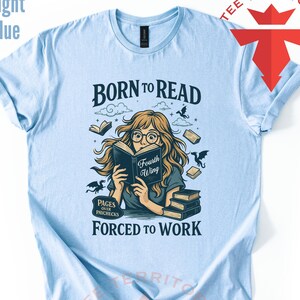 May include: Light blue t-shirt with the text "BORN TO READ" and an illustration of a person reading a book. The illustration includes the text "Fourth Wing" and "PAGES OVER PAYCHECKS FORCED TO WORK".