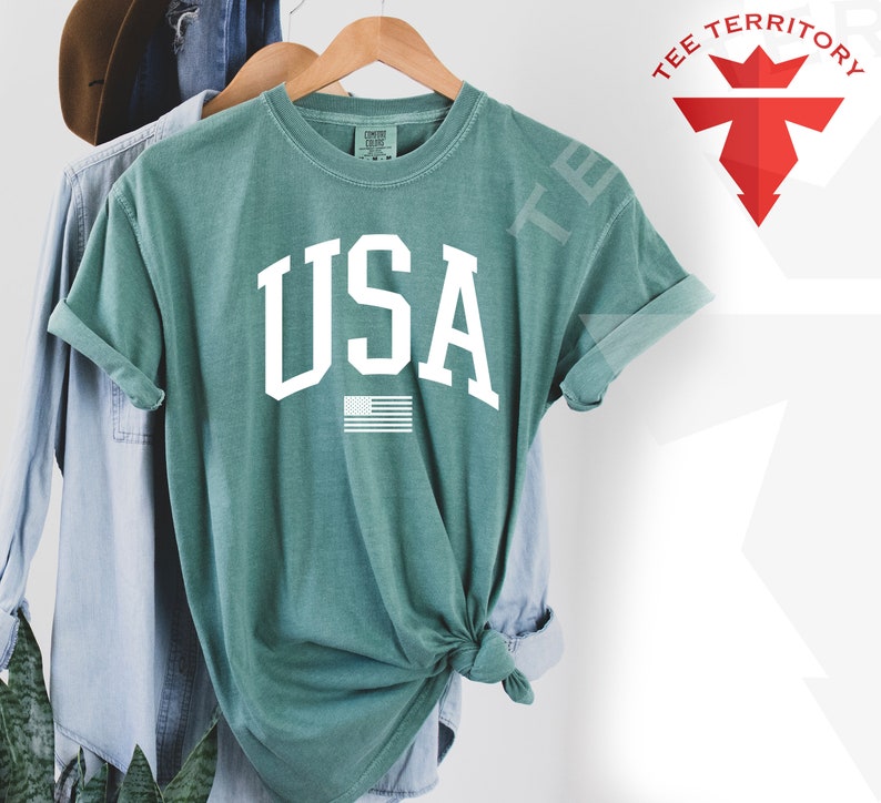 May include: A teal blue t-shirt with the word "USA" in white block letters and a small American flag graphic below.