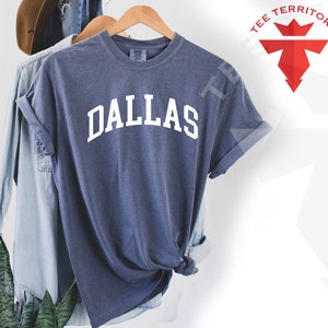 May include: A blue t-shirt with the word "DALLAS" printed in white on the front. The shirt is made of a soft, comfortable material and has a relaxed fit.