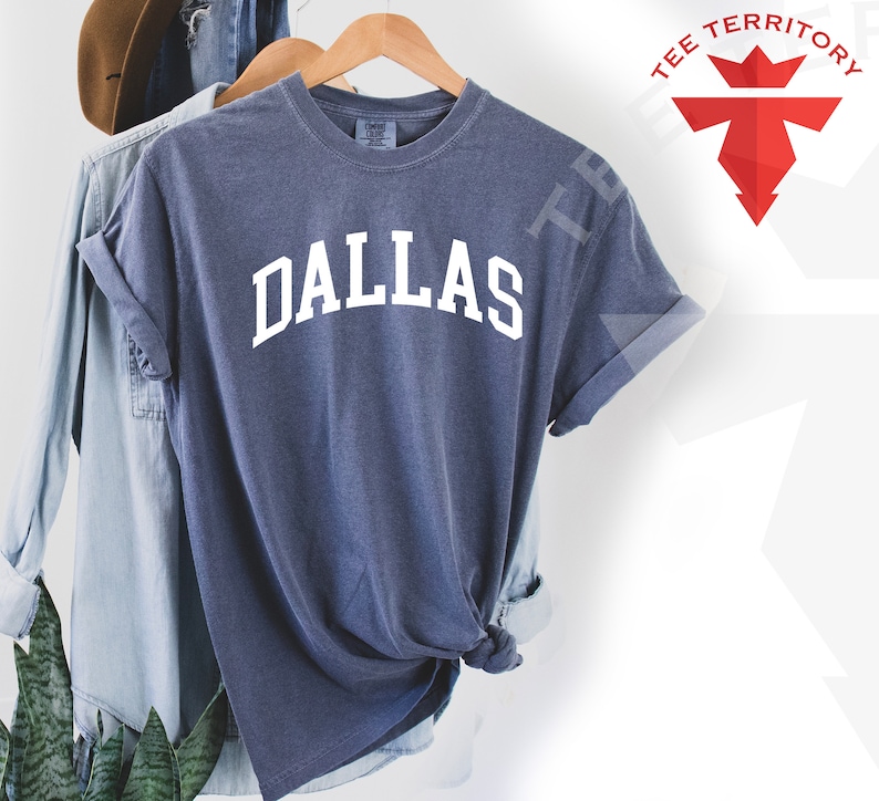 May include: A blue t-shirt with the word "DALLAS" printed in white on the front. The shirt is made of a soft, comfortable material and has a relaxed fit.