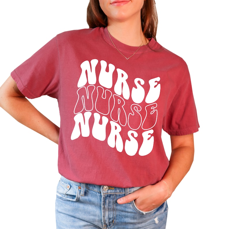 Puede incluir: Una camiseta de color granate con un gr&aacute;fico blanco de la palabra "NURSE" repetida tres veces en una fuente ondulada y psicod&eacute;lica.
