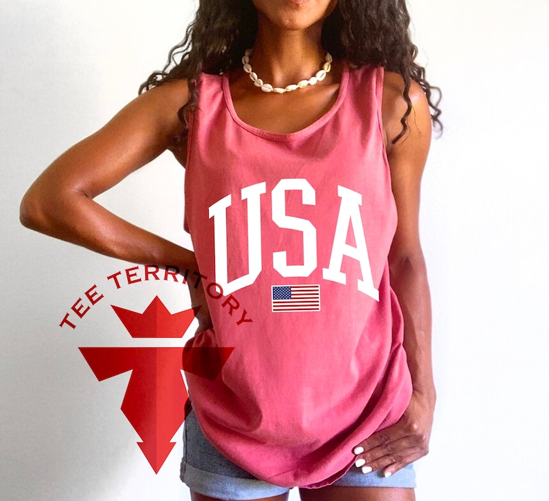 May include: A red sleeveless tank top with the word "USA" printed in white on the front. The American flag is printed below the word "USA".