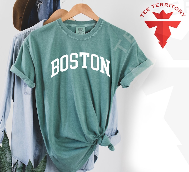 May include: A teal blue t-shirt with the word "BOSTON" printed in white on the front. The shirt is tied in a knot at the bottom.