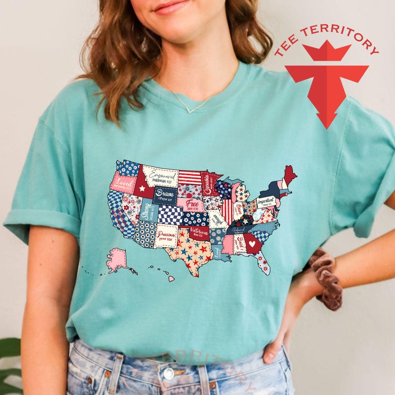 Pu&ograve; includere: Una maglietta blu turchese con un design a patchwork degli Stati Uniti d'America. Ogni stato &egrave; un motivo diverso con parole come "Brave", "Free" e "Strong" scritte su di esso.