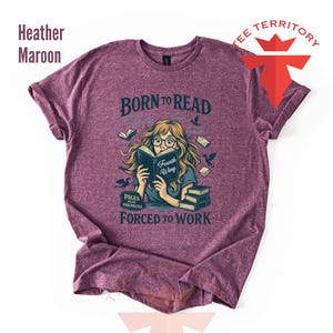 May include: Heather maroon t-shirt with the text "BORN TO READ" and a graphic of a person reading a book. The graphic also includes the text "Fourth Wing" and "PAGES OVER PAYCHECKS FORCED TO WORK".