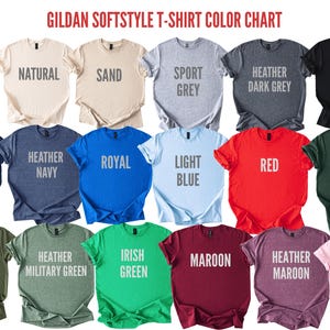 May include: Color chart of Gildan Softstyle t-shirts, showcasing various colors including white, black, navy, red, and green. Each shirt displays its color name in a bold, sans-serif font.