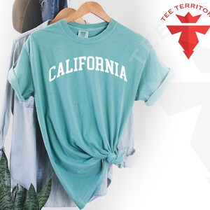 May include: A teal blue t-shirt with the word "CALIFORNIA" printed in white on the front. The shirt is tied in a knot at the bottom.