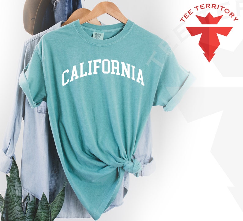 May include: A teal blue t-shirt with the word "CALIFORNIA" printed in white on the front. The shirt is tied in a knot at the bottom.