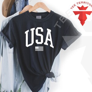 May include: Black t-shirt with a white "USA" graphic and a small American flag.