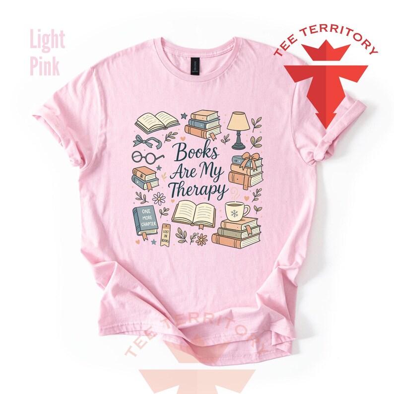 Może przedstawiać: Jasnor&oacute;żowa koszulka z napisem "Books Are My Therapy". Grafika przedstawia stosy książek, okulary, lampę i filiżankę kawy. Koszulka ma kr&oacute;tkie rękawy i okrągły dekolt.