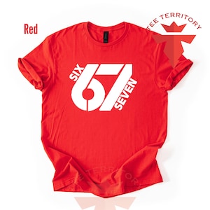 May include: A red t-shirt with the white text "SIX 67 SEVEN" printed on the front. The shirt has short sleeves and a crew neck. The words "TEE TERRITORY" are printed on the top right.