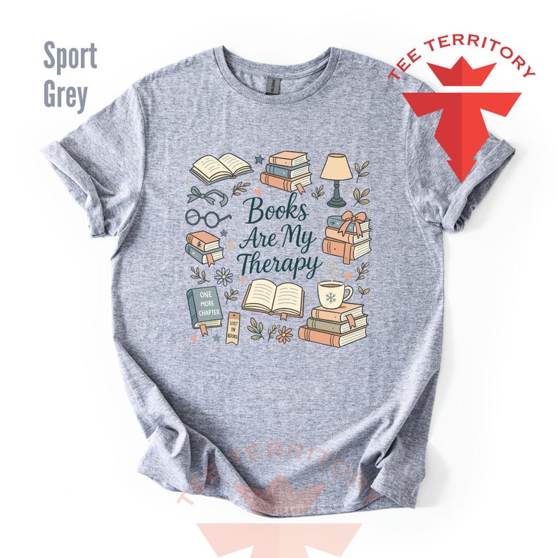 Może przedstawiać: Szara koszulka sportowa z kolorowym wzorem graficznym przedstawiającym książki, okulary, lampę i napis "Books Are My Therapy". Projekt zawiera filiżankę kawy, kwiaty i słowa "One More Chapter".