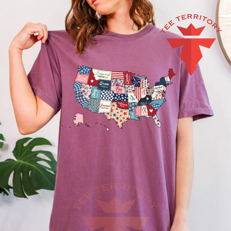 Pu&ograve; includere: Una maglietta viola con un design a patchwork degli Stati Uniti. Ogni stato &egrave; un motivo diverso con parole come "Strong", "Free" e "Brave" su di esso.