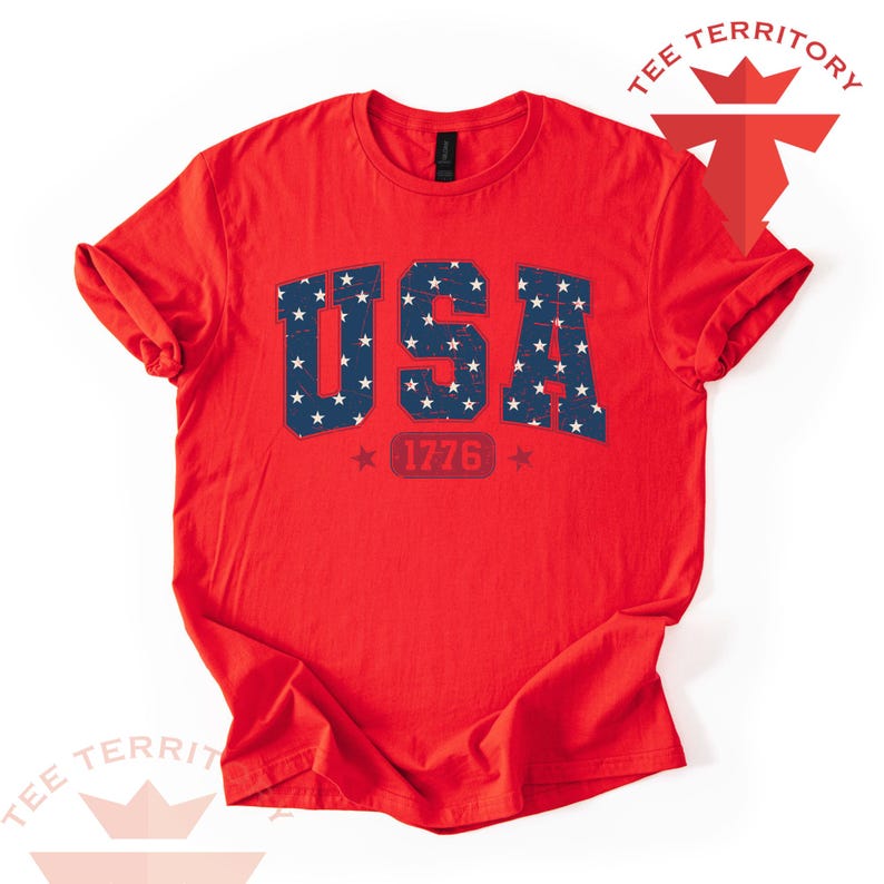 May include: A red t-shirt with the word "USA" in blue, filled with white stars. Below the word "USA" is the number "1776" in red, with a star on each side. The shirt has rolled-up sleeves.