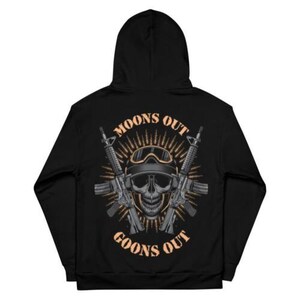 May include: Black hooded sweatshirt with a graphic on the back. The graphic features a skull wearing goggles, crossed rifles, and the text "MOONS OUT GOONS OUT" in a stylized font. The design is in shades of gray and tan.