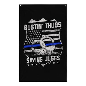 May include: Black and white flag with a blue stripe and handcuffs. The flag has a shield shape with the text "Bustin' Thugs Saving Juggs" and stars.