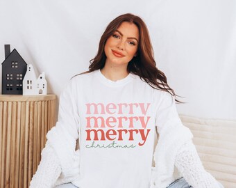 May include: A white long-sleeved shirt with a pink and red "merry" graphic repeated three times and the text "christmas" in green below.