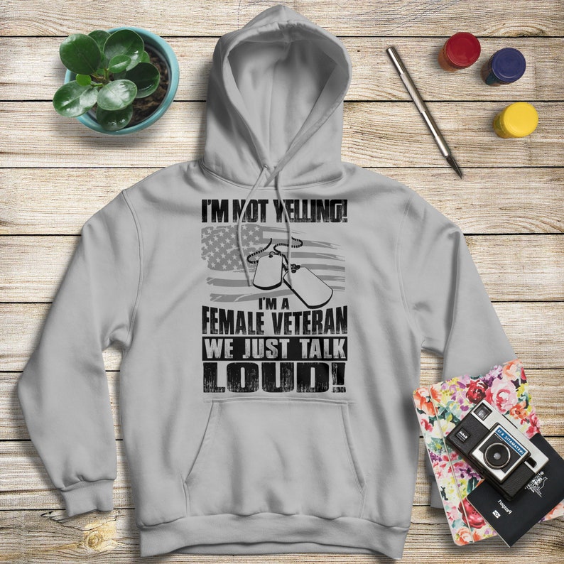 May include: A gray hooded sweatshirt with the text "I'm not yelling! I'm a female veteran we just talk loud!" printed on the front. The text is in black and is surrounded by a small American flag graphic and two dog tags.