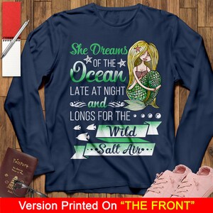 May include: Navy blue long-sleeve shirt with a mermaid illustration and the text "She Dreams of the Ocean Late at Night and Longs for the Wild Salt Air".