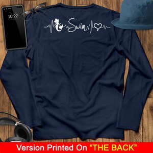 Puede incluir: Camiseta de manga larga azul marino con un gr&aacute;fico de sirena blanca y el texto "Swim" en un dise&ntilde;o de latido del coraz&oacute;n. El dise&ntilde;o est&aacute; impreso en la parte posterior de la camiseta.