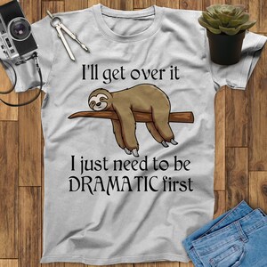 May include: A gray t-shirt with a cartoon sloth hanging from a branch. The text on the shirt reads "I'll get over it I just need to be DRAMATIC first."