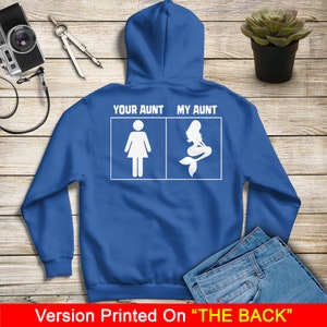 Puede incluir: Una sudadera con capucha azul real con texto blanco que dice "Your Aunt" y "My Aunt" con una silueta de una mujer y una sirena en las casillas debajo del texto. El texto est&aacute; impreso en la parte posterior de la sudadera con capucha.