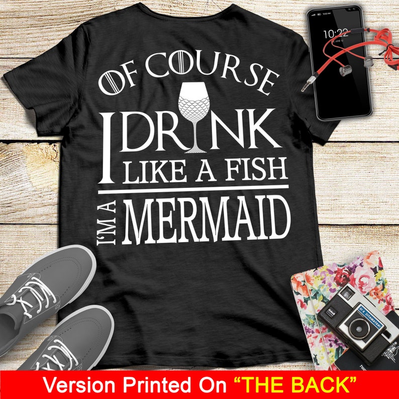 May include: Black t-shirt with white text that reads "Of course I drink like a fish I'm a mermaid". The text is surrounded by a white outline. A wine glass with a mermaid tail design is in the middle of the text.