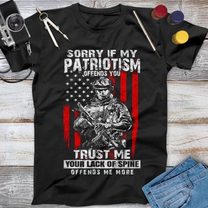 May include: Black t-shirt with a white graphic of a soldier holding a rifle in front of an American flag. The text reads "Sorry if my patriotism offends you. Trust me your lack of spine offends me more."